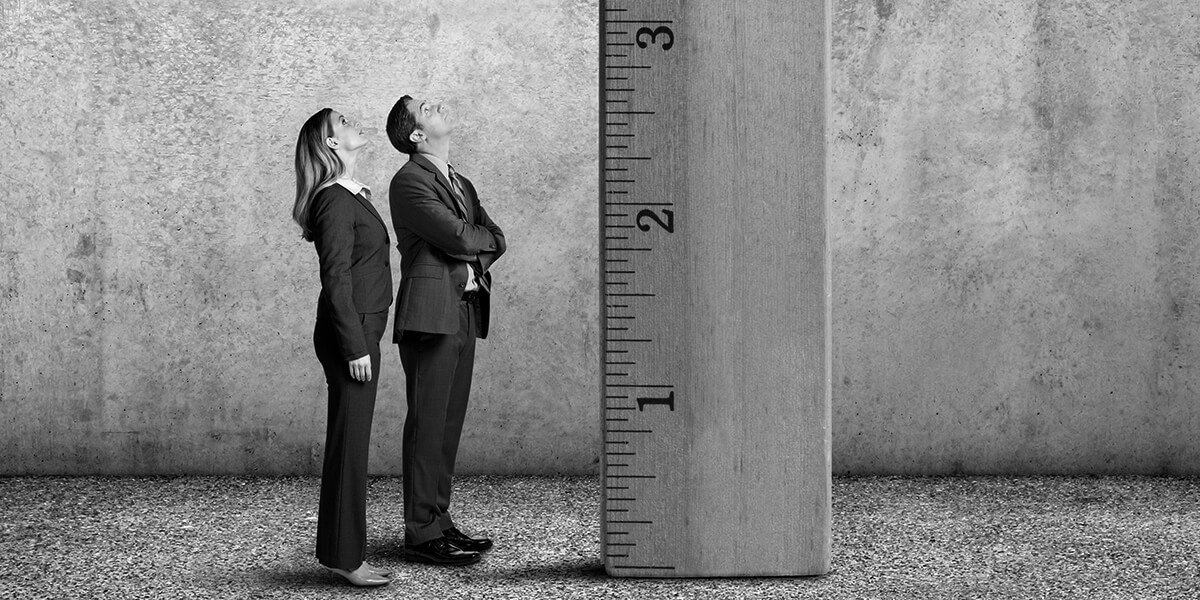 Two tiny people standing beside a giant ruler staring up, the people measure just over 2 inches in height.