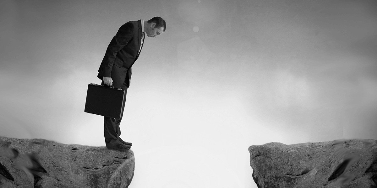 Man with briefcase looking down into chasm.